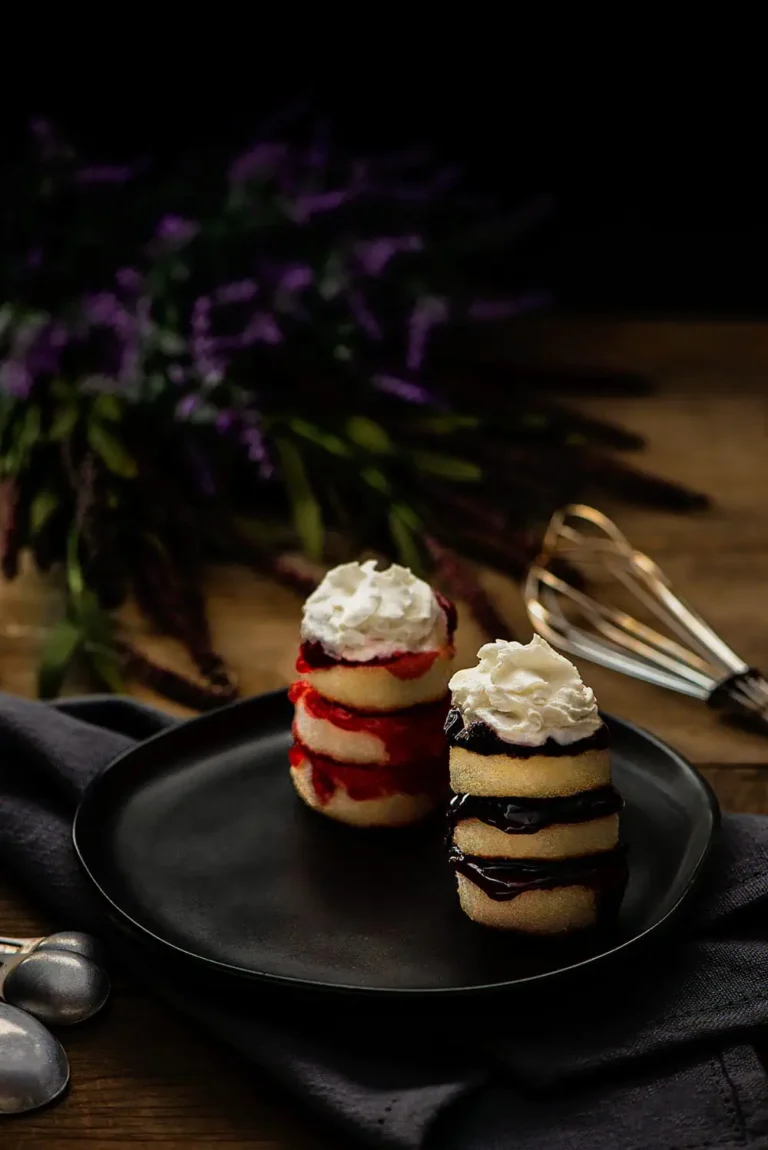 Heavenly angel food cake, two stacked angel food cakes on a black plate with purple flowers in the background and a whisk.