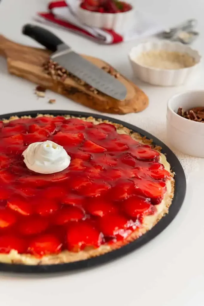 Strawberry Pizza in a round flat pizza pan with a dollop of whipped topping in the center.