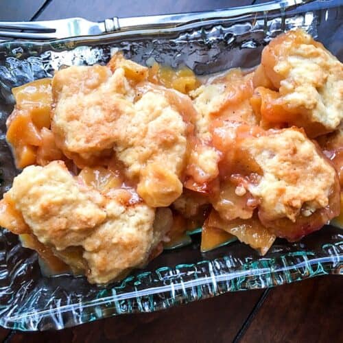 Peach cobbler in a dish sitting on a table with a fork beside it