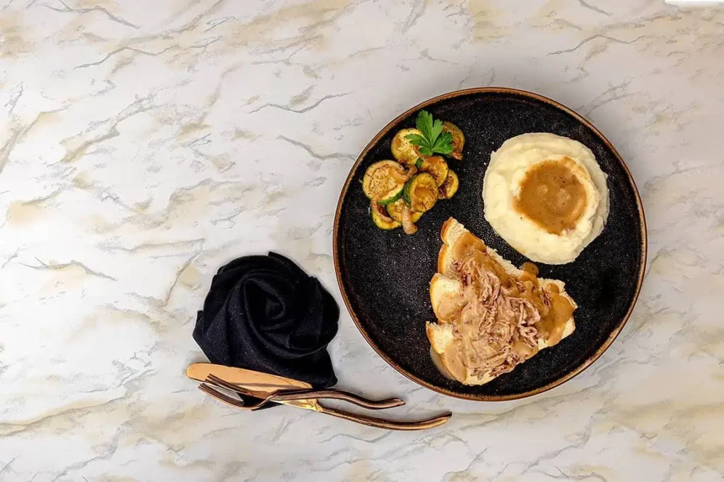plate filled with delicious open faced tri tip sandwich, mashed potatoes and gravy you'll love, and sauted zucchini