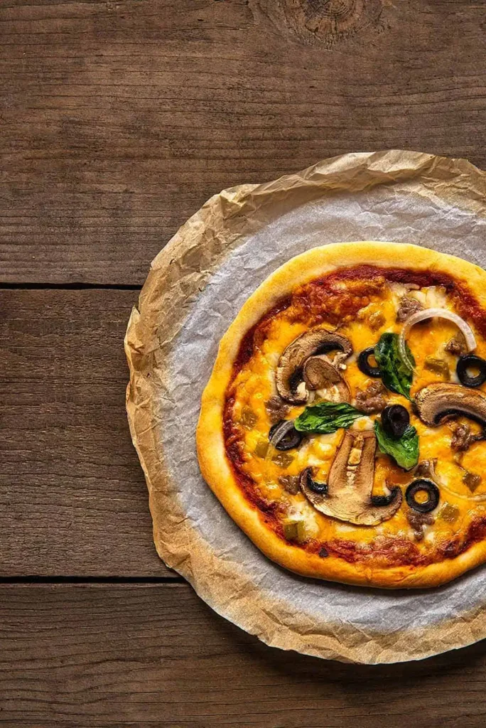 One pizzeria style pizza baked and cooling on parchment paper and setting on a wooden grape tray