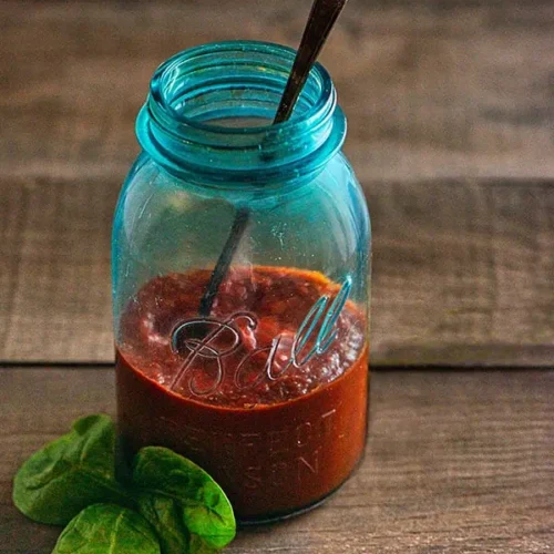 A mason jar filled with pizza sauce, sitting on a wooden grape tray