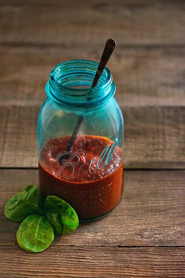 A mason jar filled with pizza sauce, sitting on a wooden grape tray