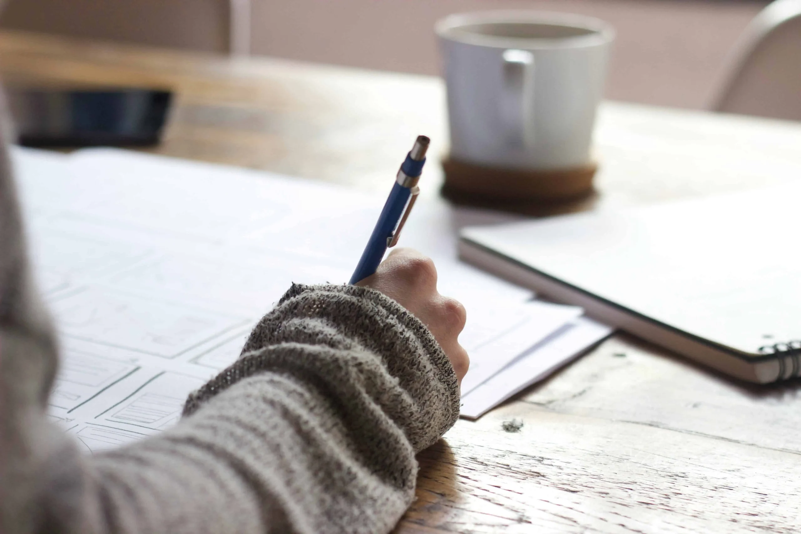 Journaling Techniques for a better you a woman sitting at a table writing in a journal. also on the table are notebooks, coffee cup and papers