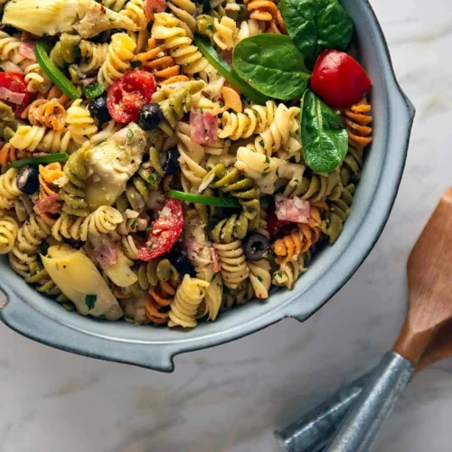 Pasta Salad Easy and Italian. A blue bowl filled with Pasta Salad and in the lower left are two serving spoons.