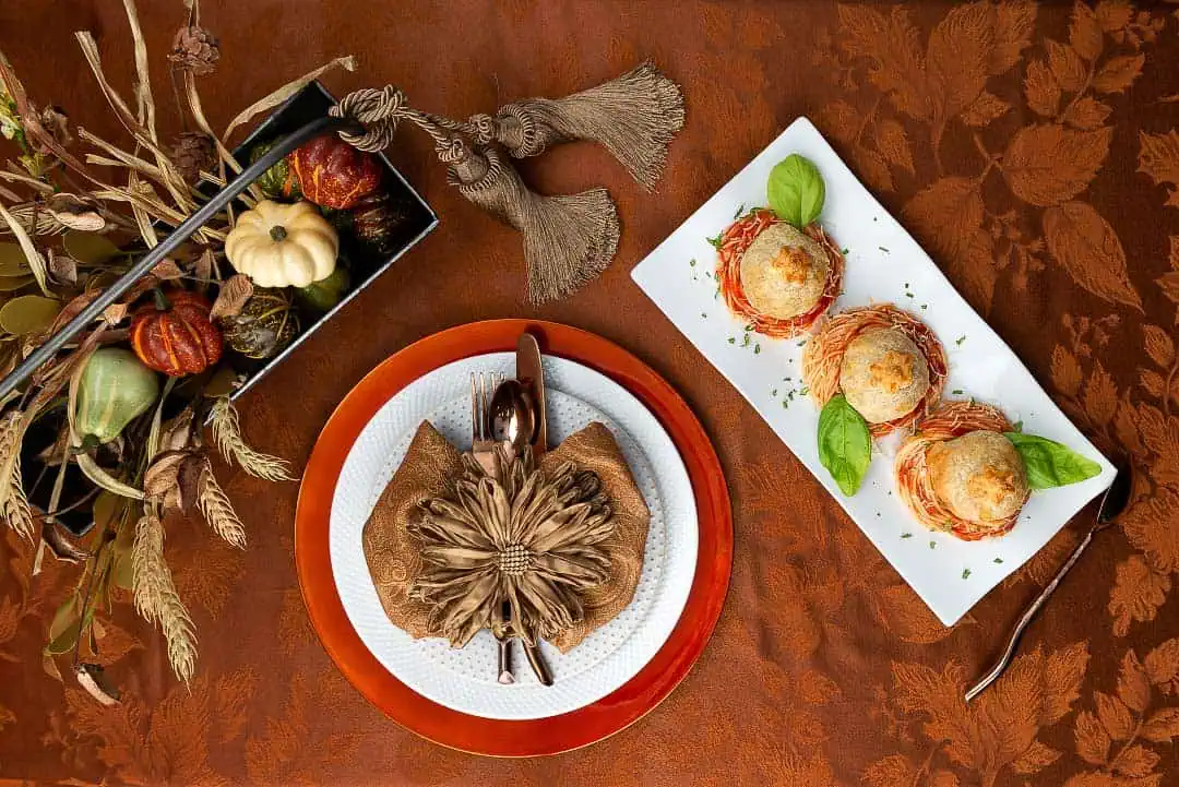 Delectable & Delicious Meatball Wellington An overhead shot of a Thanksgiving Table. On the table is a centerpiece, charger, plate and topped with a napkin and silverware. Also, there is a serving platter of swirled pasta and topped with meatball wellington.