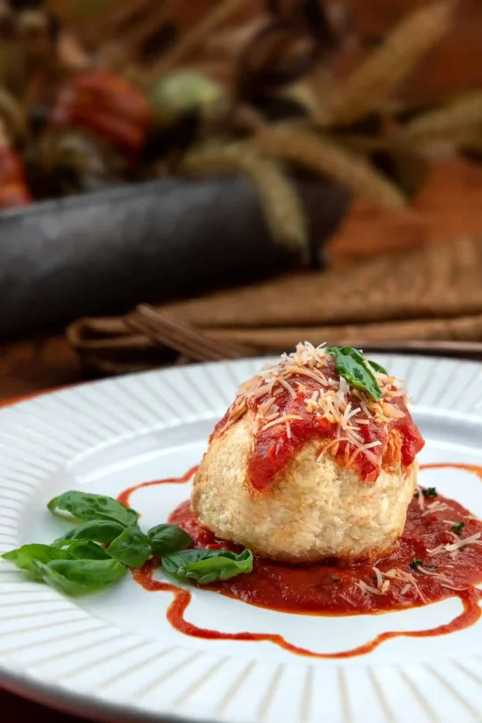 Delectable & Delicious Meatball Wellington An side view close-up view of meatball wellington sitting on top of spaghetti sauce and garnished with basil.