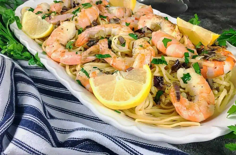 Shrimp Scamp and Veggies Over Pasta. A serving plate filled with a layer of pasta, shrimp, veggies and sliced lemons.