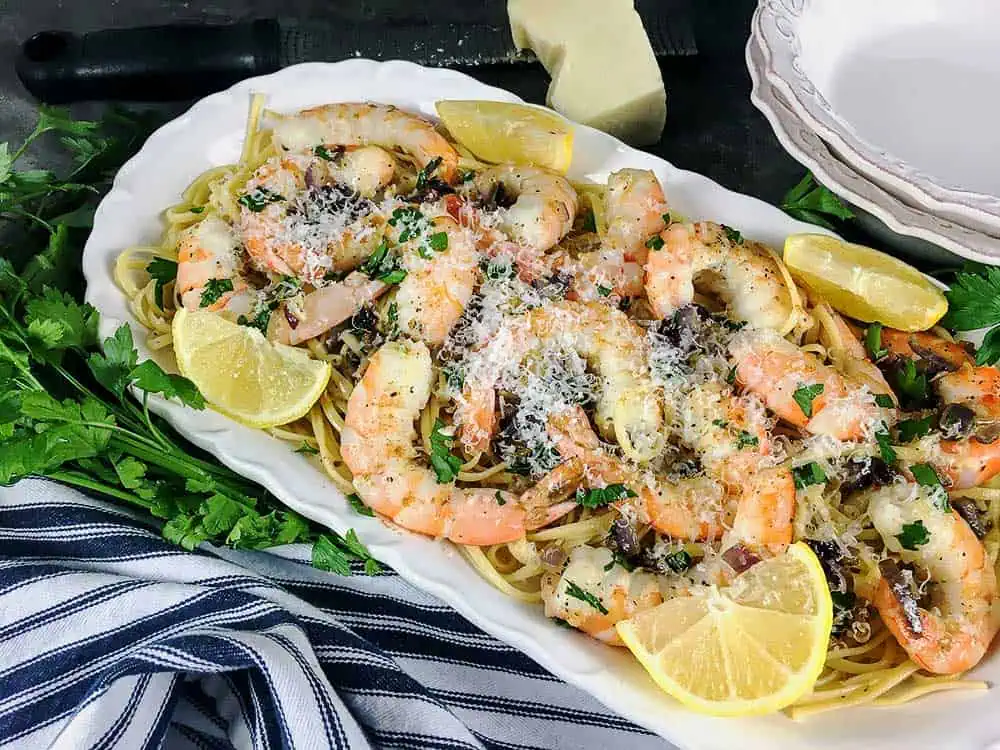 Easy Shrimp Scampi and Veggies Over Pasta. A serving plate filled with a layer of pasta, shrimp, veggies and sliced lemons.