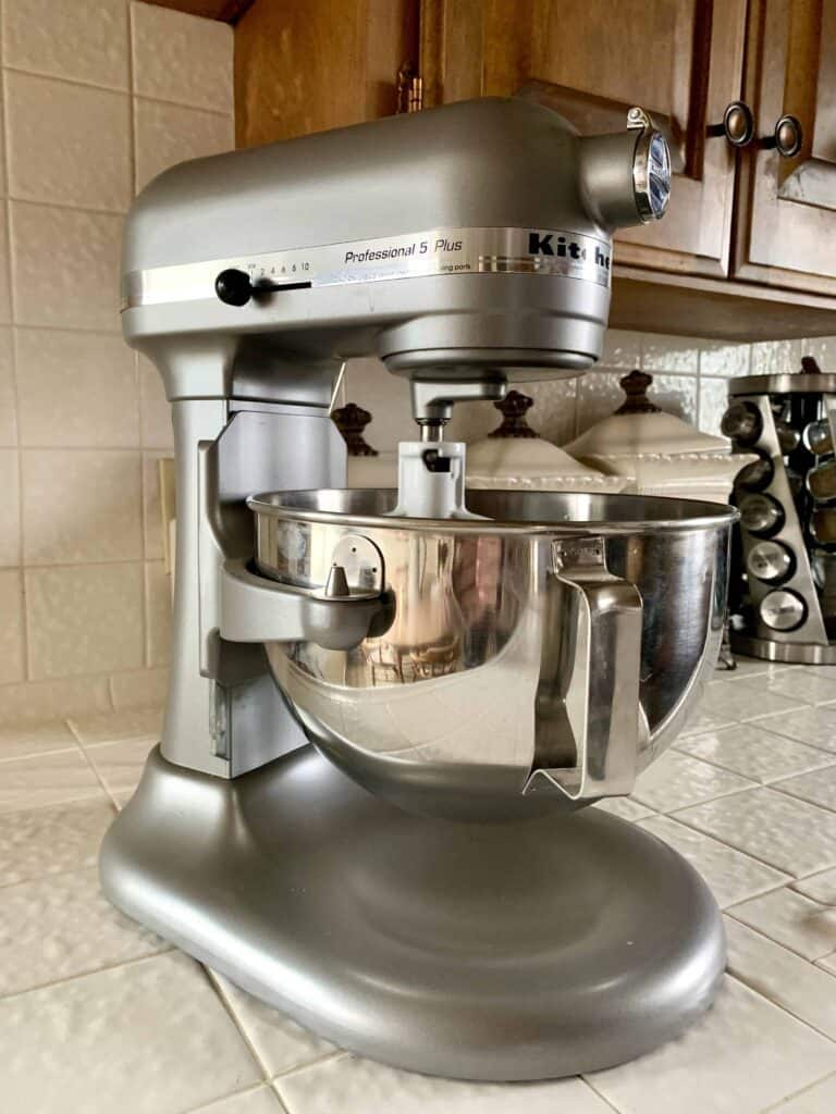 Stand Mixer_1 KitchenAid Professional 5 Plus stand mixer in metallic silver, placed on a tiled kitchen counter. The mixer features a large stainless steel mixing bowl and a paddle attachment, ready for use.