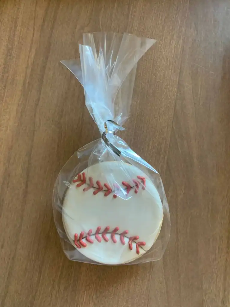 A single decorated baseball sugar cookie packaged in a clear treat bag and sealed with a silver twist tie