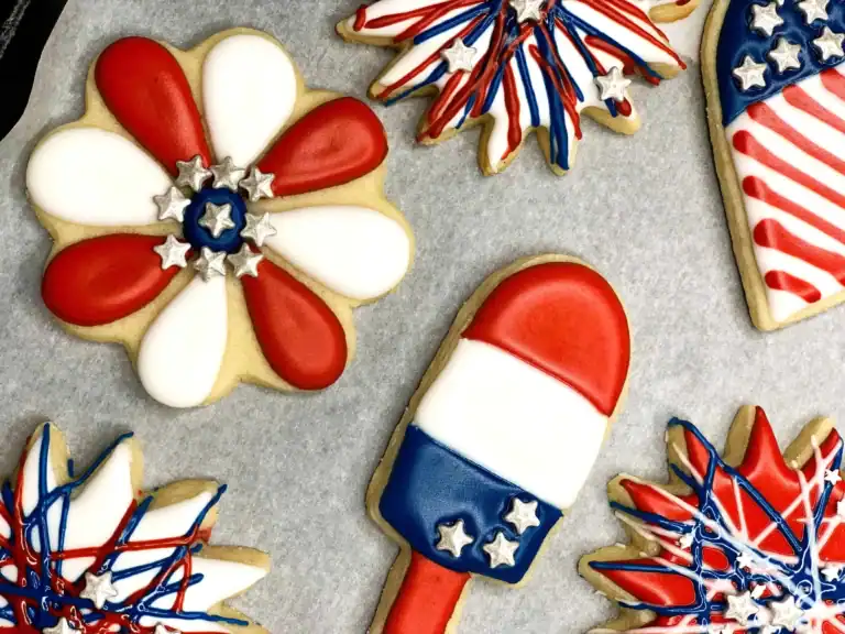 Close-up of 4th of July sugar cookies including a red and white flower, patriotic popsicle, and firework designs decorated with royal icing.