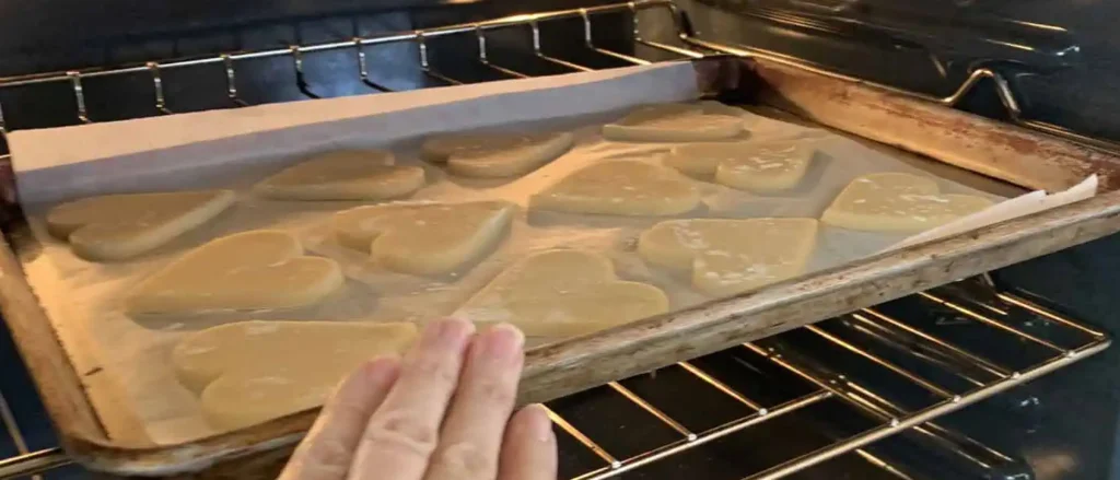A tray of flash frozen heart-shaped sugar cookie dough is being placed into an oven to bake. The dough is evenly spaced on parchment paper for consistent baking and shape retention.