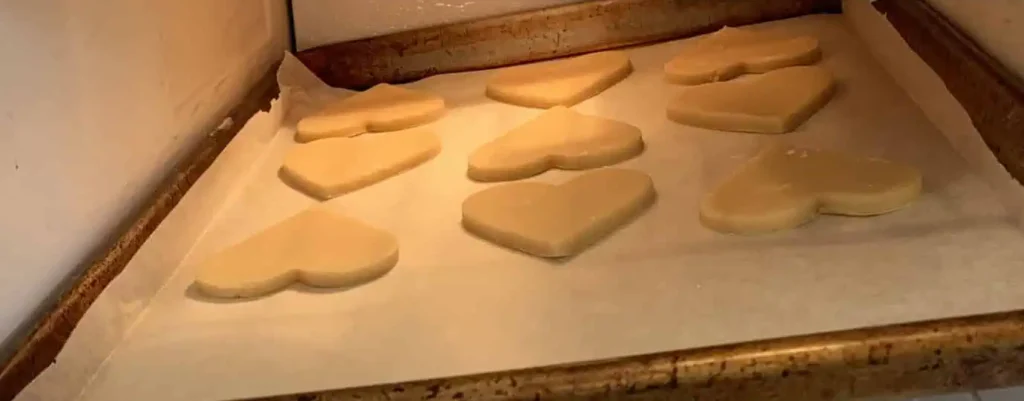 Heart-shaped sugar cookie dough cutouts on a parchment-lined baking sheet placed in the freezer. The cookies are being flash frozen to help maintain their shape during baking.
