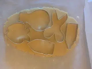 Back-to-school cookie cutters placed on rolled sugar cookie dough, including shapes for a pencil, scissors, apple, pen, and hot air balloon.