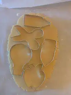 Back-to-school cookie cutters placed on rolled sugar cookie dough, including shapes for a pencil, scissors, apple, pen, and hot air balloon.