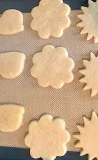 Tray of unbaked sugar cookie dough in floral and firework shapes on a baking mat, ready for decorating.