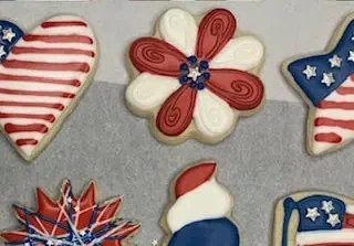 Close-up of a red and white flower-shaped sugar cookie decorated with royal icing in a 4th of July theme.