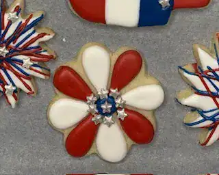 Tray of 4th of July-themed sugar cookies decorated in red, white, and blue with designs including fireworks, flowers, popsicles, flags, hearts, and patriotic sunglasses.