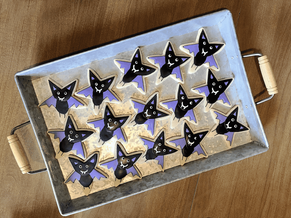 Halloween sugar cookie decorated with royal icing as a cute vampire on a star-shaped cookie with purple wings and fangs.