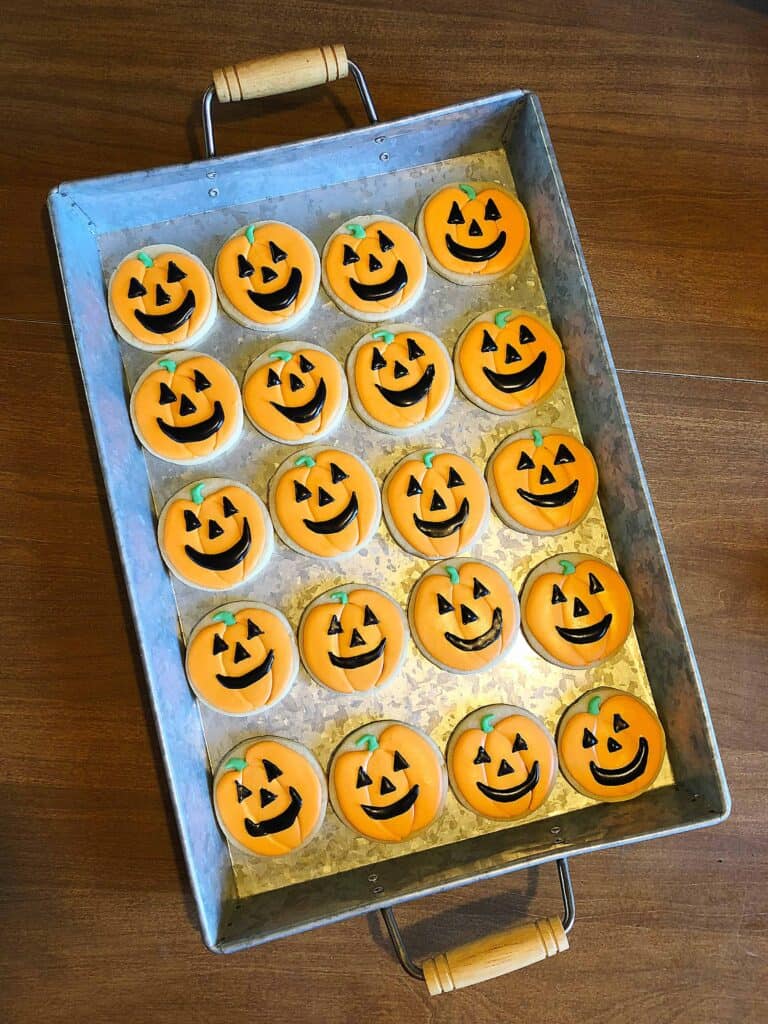 Round Halloween sugar cookie decorated with royal icing as a smiling jack-o-lantern face in orange and black.