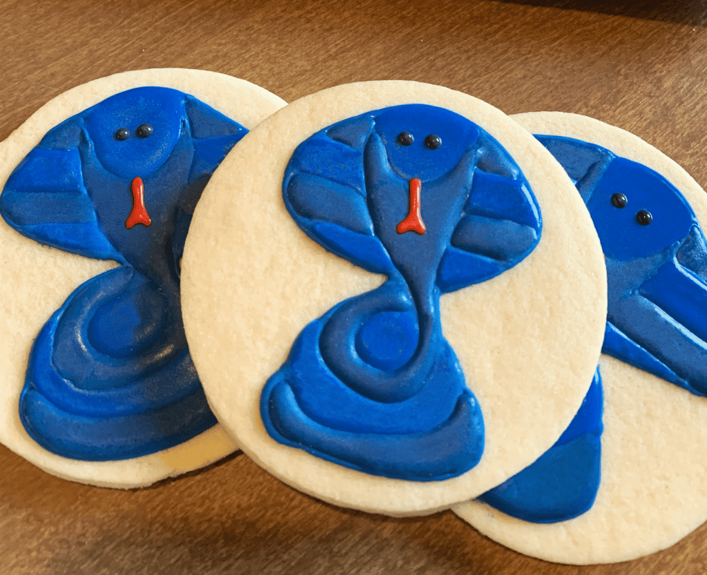 Halloween sugar cookie decorated with royal icing as a blue cobra with black eyes and a red tongue.