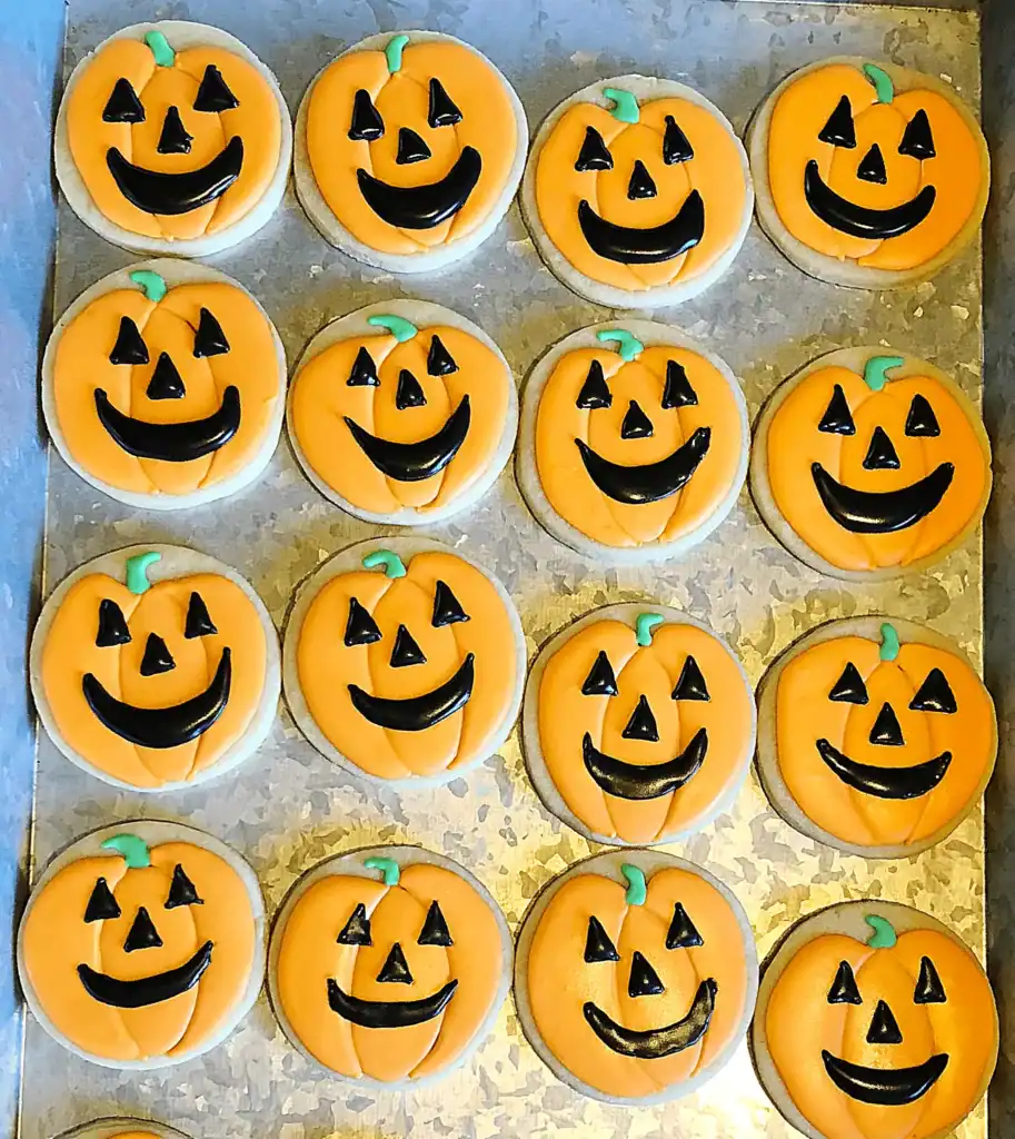 Round Halloween sugar cookie decorated with royal icing as a smiling jack-o-lantern face in orange and black.