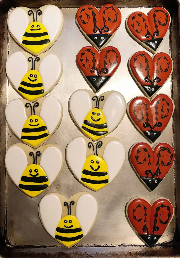 Heart-shaped Halloween sugar cookie decorated with royal icing as a bumble bee with yellow and black stripes, white wings, and a smiley face