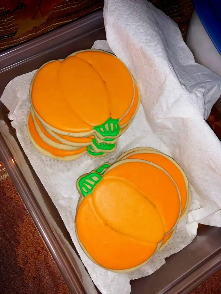 Pumpkin-shaped Halloween sugar cookie decorated with orange royal icing and a green stem.