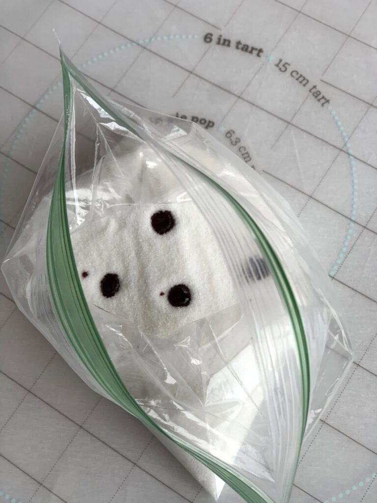 White sugar in a plastic baggie with 3 dots of red food coloring.