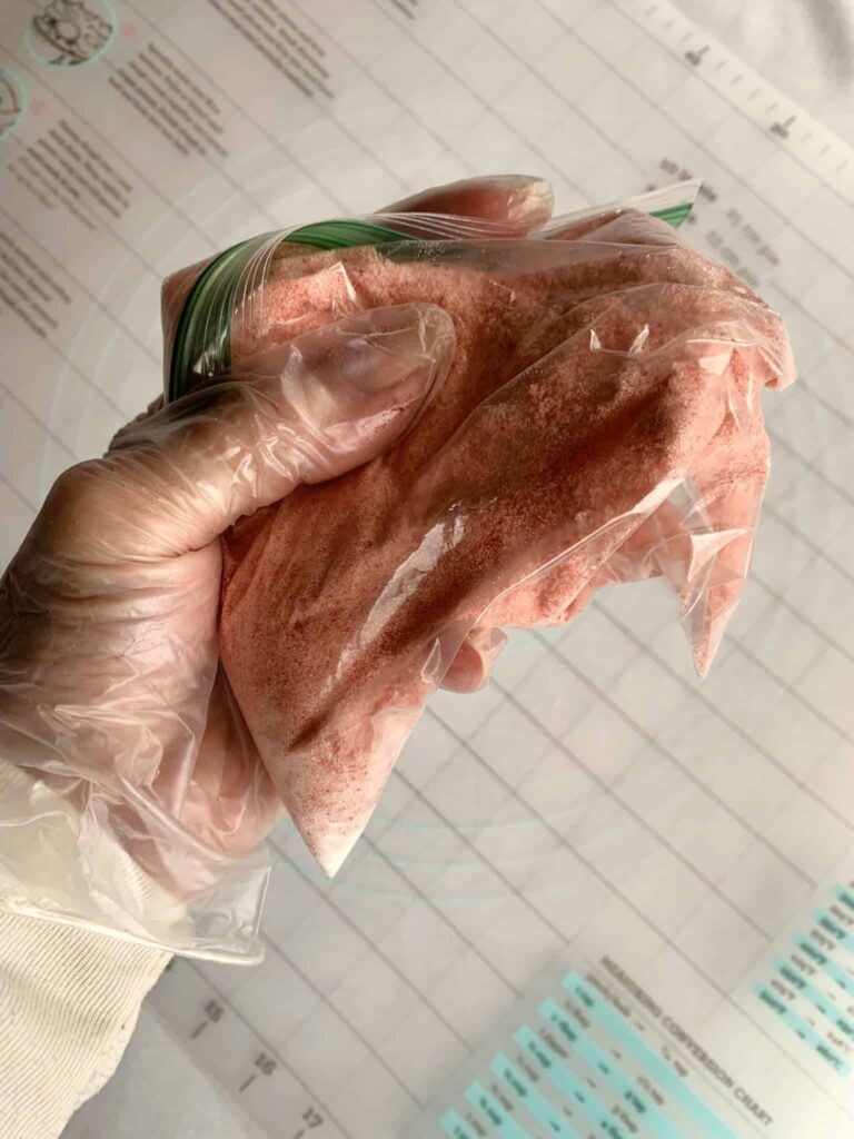 Sanding sugar in a plastic bag with red food coloring being mixed together.