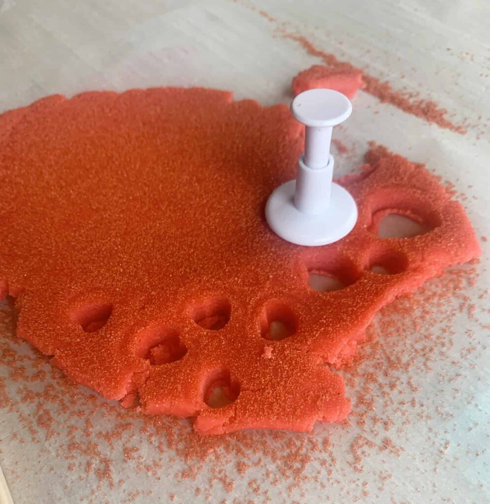 Using a cookie cutter to cut small hearts from red sugar cookie dough.