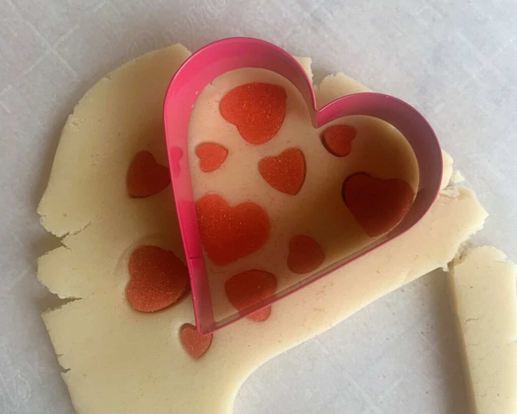Natural color sugar cookie dough in heart shape with red heart inset pattern.