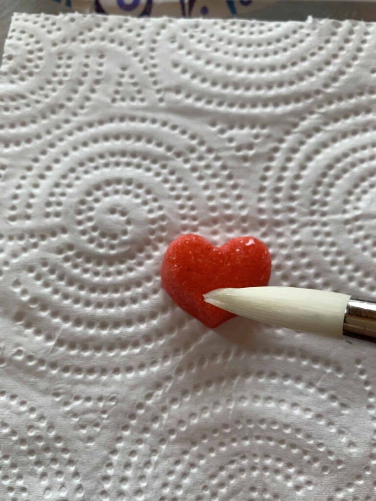 Applying karo syrup to small heart bite sugar cookie.
