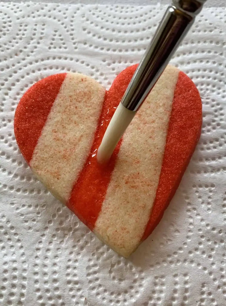 Heart shaped sugar cookie with alternating striped dough and applying karo syrup.