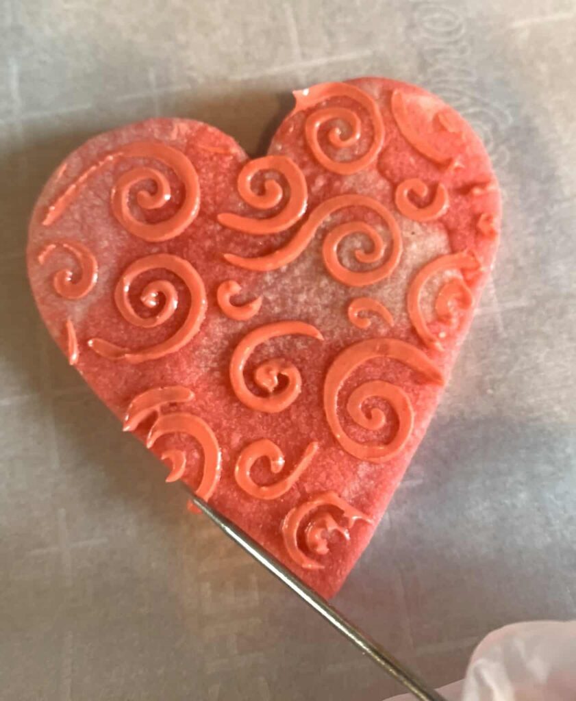 Heart shaped sugar cookies with royal icing stenciled with a swirling pattern design.