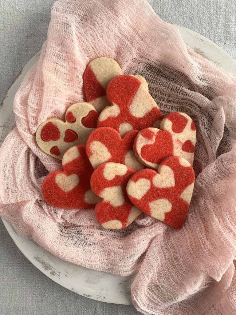 Heart shaped sugar cookies on a wood serving tray with a heart shaped dough pattern.