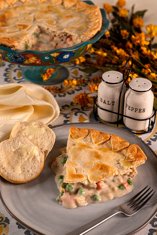 Classic Chicken Pot Pie - a dinner plate with a large slice of chicken pot pie, biscuits, salt and pepper shaker.