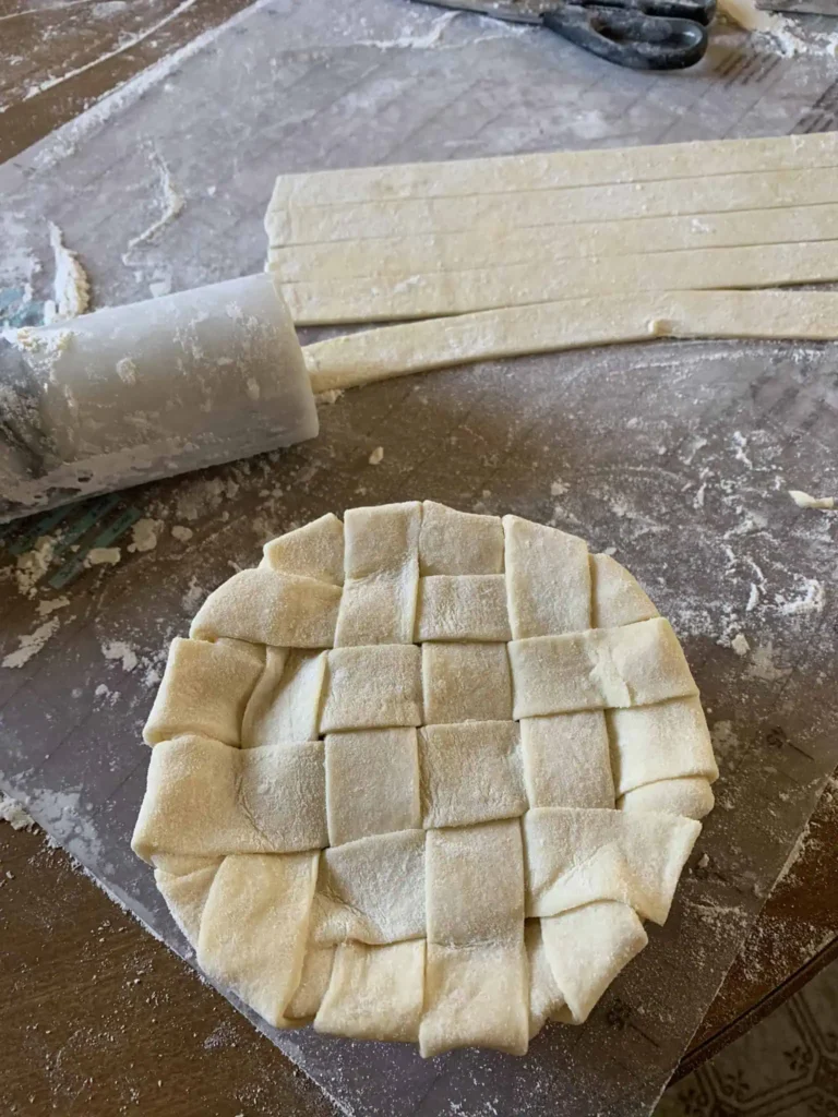 Rolled out best flaky pie dough cut into strips on a floured work surface, with a pie that is ready to bake.